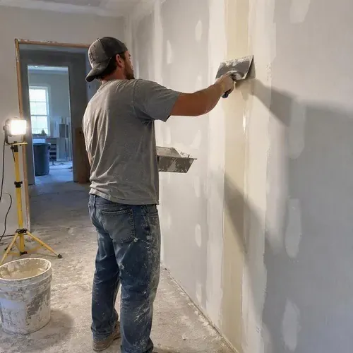 Worker spreading second mud coat on seam during drywall taping and finishing in Kingston, ON