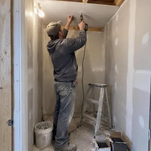 Worker screwing drywall to closet ceiling joists on a residential drywall installation in Kingston, ON