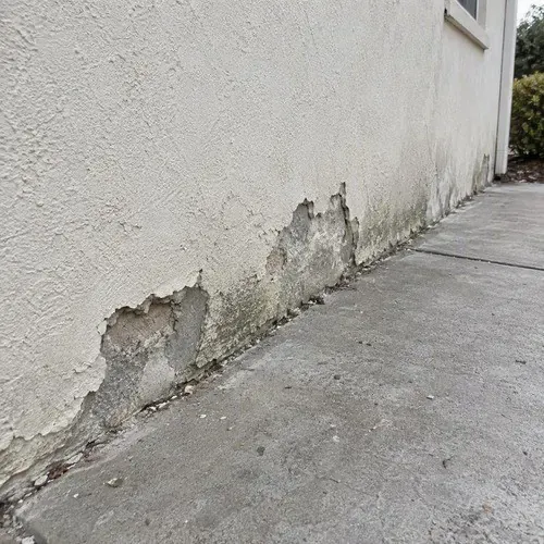 Chipped stucco at wall base near walkway on a stucco repair job in the Kingston area